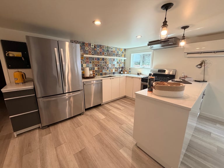 Modern kitchen with stainless steel appliances, white cabinetry, central island, wood-look flooring, and pendant lighting