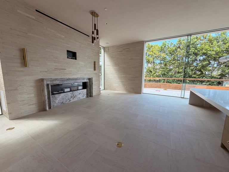 Empty modern living room with light wood flooring, fireplace, and large windows overlooking trees