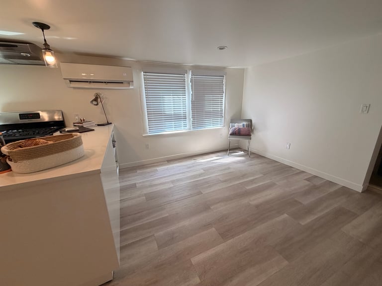 Modern apartment interior with open floor plan showing kitchen with island, wood-look flooring, and living area with large windows