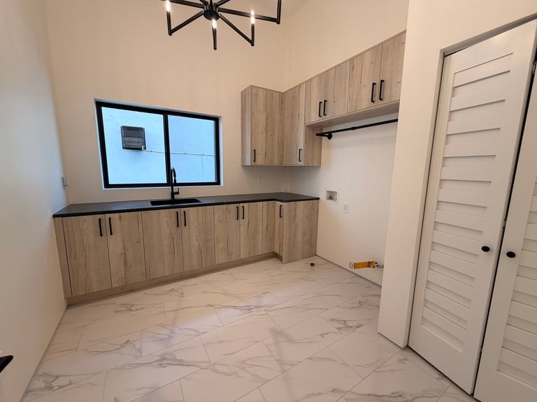 Modern kitchen with wood cabinetry, double windows above counter, marble tile flooring, and white closet doors