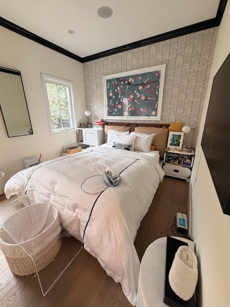 Modern bedroom with white bedding, wooden headboard, patterned accent wall, window, and contemporary furnishings
