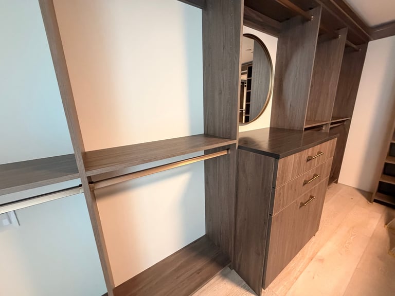Modern walk-in closet with dark wood cabinetry, shelving, mirror, and warm lighting