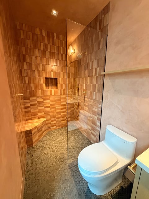 Modern bathroom with walk-in shower featuring orange tile walls, glass enclosure, and a white toilet