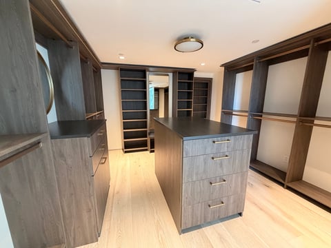 Modern walk-in closet with dark wood cabinetry, island drawers, built-in shelving, and light wood flooring