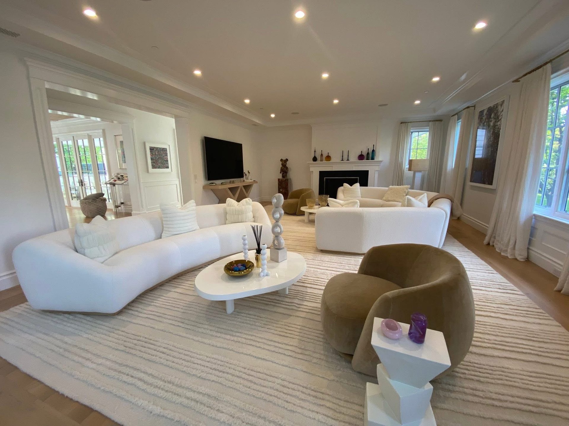 Spacious modern living room with white curved furniture, olive green chair, and recessed lighting