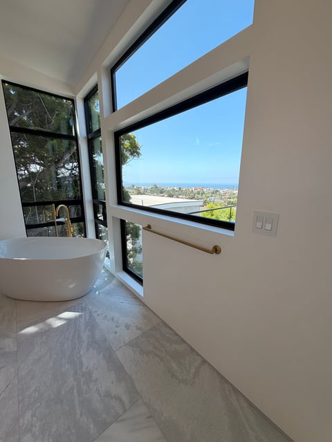 Modern bathroom with freestanding white bathtub, floor-to-ceiling windows, and panoramic city view from hillside home